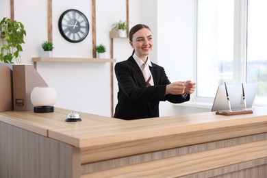 Photo of Smiling receptionist in uniform giving card key at reception desk in hotel