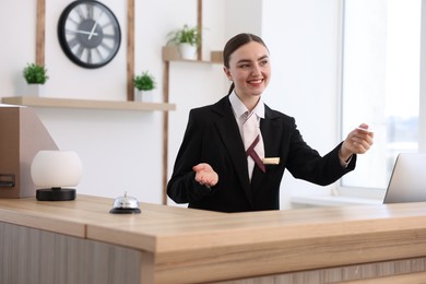 Photo of Smiling receptionist in uniform giving card key at reception desk in hotel