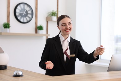 Photo of Smiling receptionist in uniform giving card key at reception desk in hotel