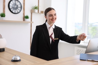 Photo of Smiling receptionist in uniform giving card key at reception desk in hotel
