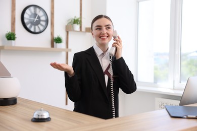 Photo of Smiling receptionist talking with client by phone at reception desk in hotel