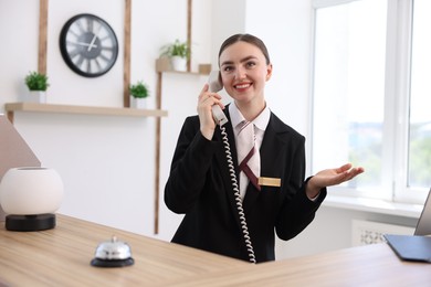Photo of Smiling receptionist talking with client by phone at reception desk in hotel