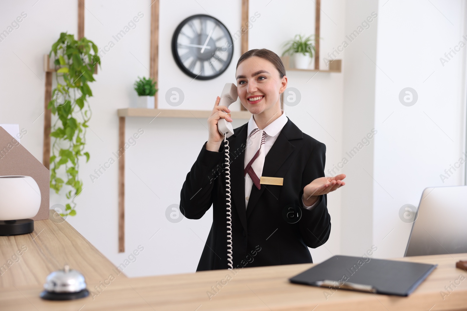 Smiling receptionist talking with client by phone at reception desk in hotel Photo of Smiling receptionist talking with client by phone at reception desk in hotel