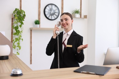 Photo of Smiling receptionist talking with client by phone at reception desk in hotel