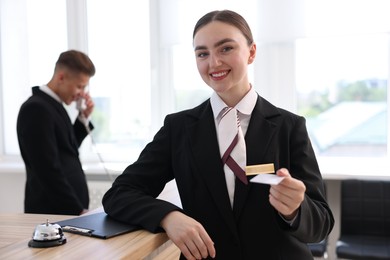 Photo of Smiling receptionist in uniform giving key card and her colleague working in hotel, selective focus