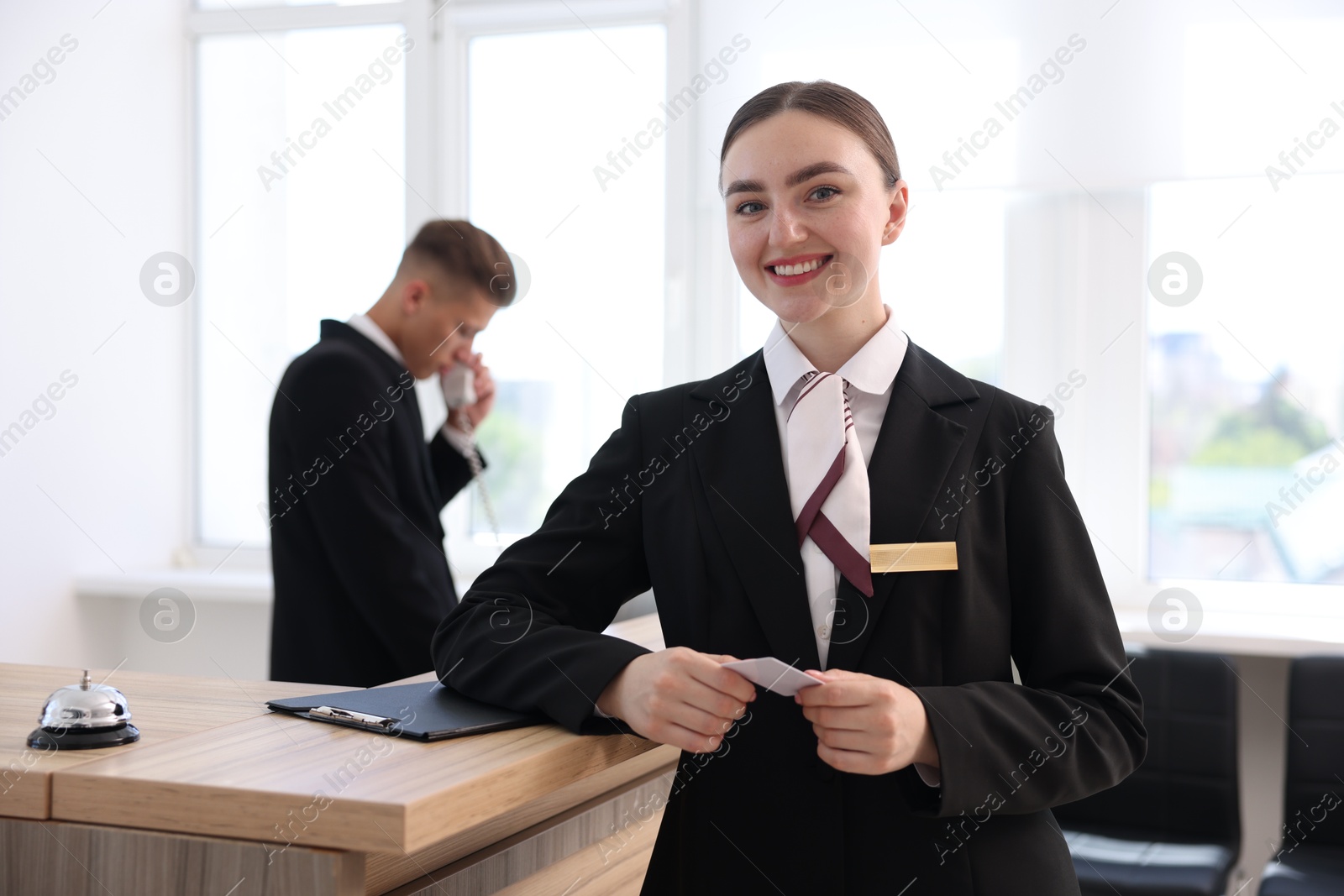 Smiling receptionist in uniform with key card and her colleague working in hotel, selective focus Photo of Smiling receptionist in uniform with key card and her colleague working in hotel, selective focus