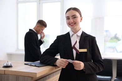 Photo of Smiling receptionist in uniform with key card and her colleague working in hotel, selective focus