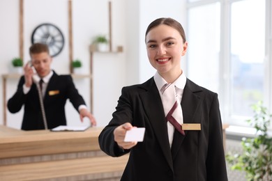 Photo of Smiling receptionist in uniform giving key card and her colleague working in hotel, selective focus