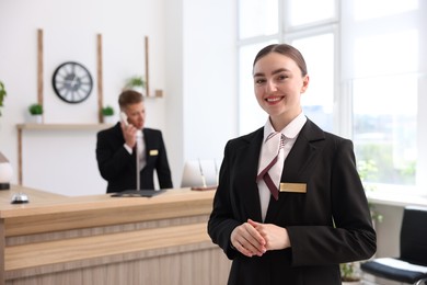 Photo of Smiling receptionist in uniform and her colleague working in hotel, selective focus