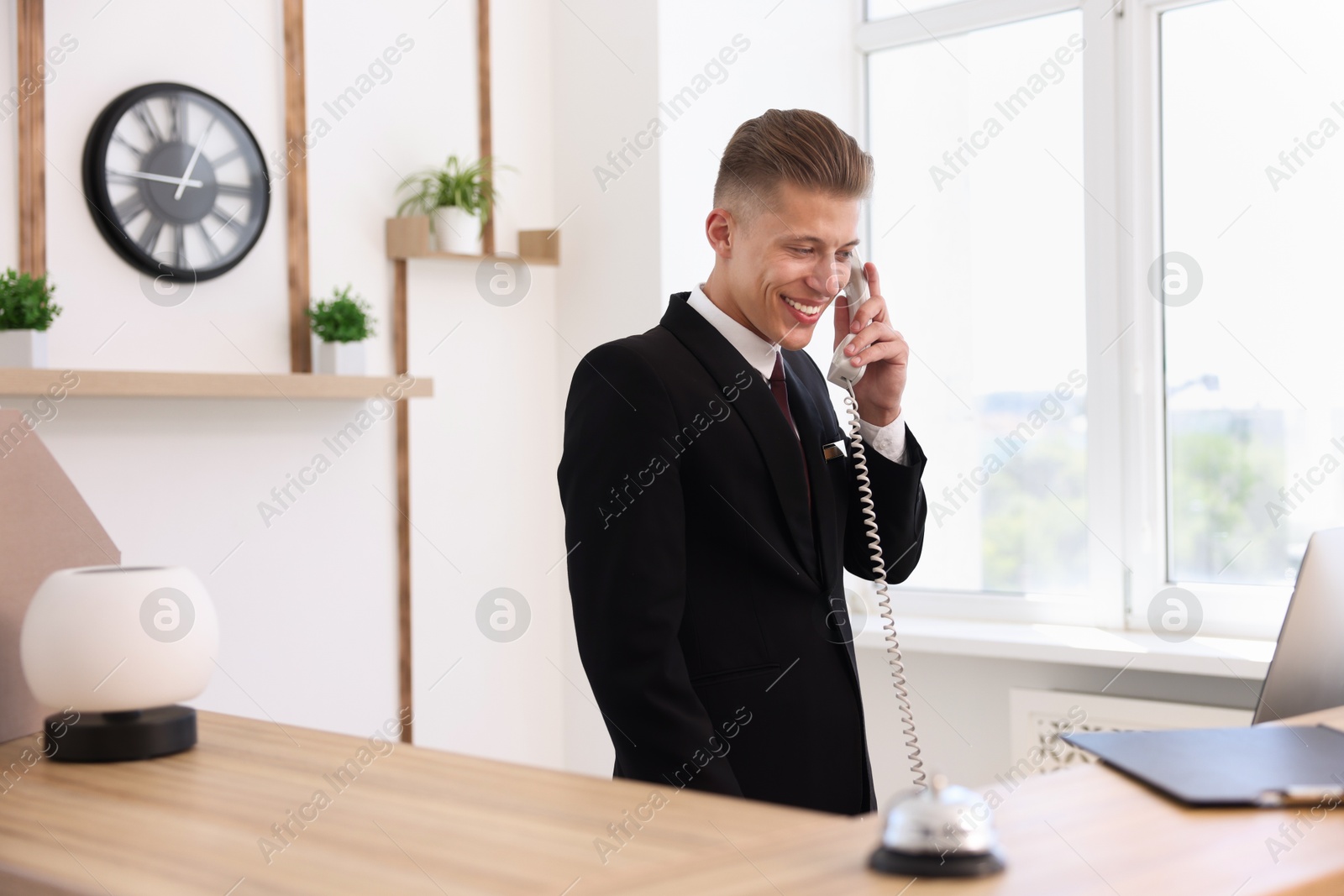 Smiling receptionist talking with client by phone at reception desk in hotel Photo of Smiling receptionist talking with client by phone at reception desk in hotel
