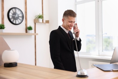 Photo of Smiling receptionist talking with client by phone at reception desk in hotel