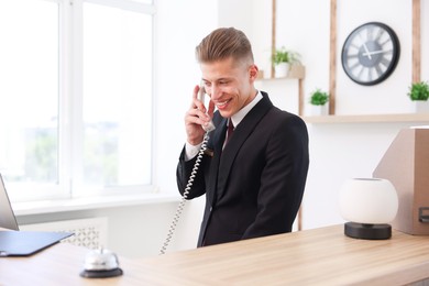 Photo of Smiling receptionist talking with client by phone at reception desk in hotel