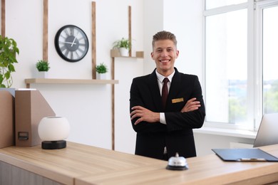 Photo of Portrait of smiling receptionist with crossed arms at reception desk in hotel