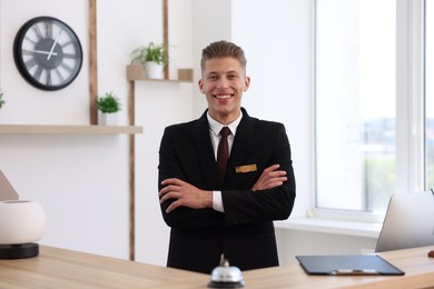 Photo of Portrait of smiling receptionist with crossed arms at reception desk in hotel