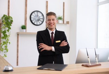 Photo of Portrait of smiling receptionist with crossed arms at reception desk in hotel