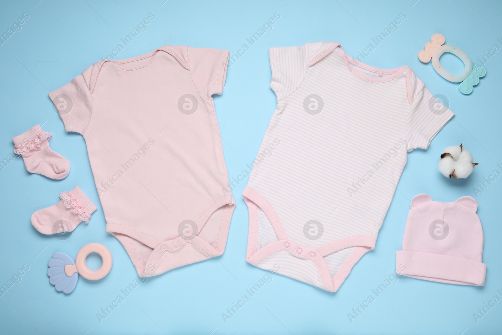 Photo of Baby clothes, cotton flower and accessories on light blue background, flat lay