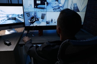 Photo of Security guard monitoring CCTV cameras in office at night, back view