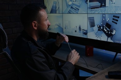 Photo of Security guard monitoring CCTV cameras and using microphone in office at night