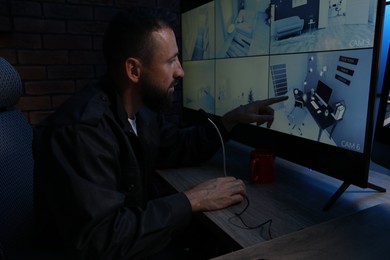 Photo of Security guard monitoring CCTV cameras and using microphone in office at night