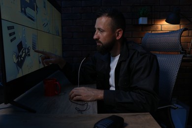 Photo of Security guard monitoring CCTV cameras and using microphone in office at night