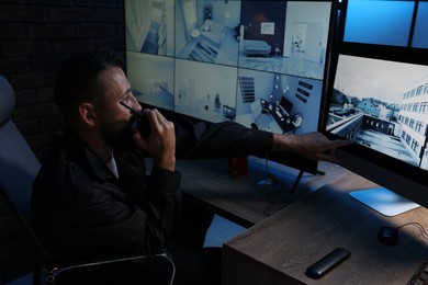 Photo of Security guard monitoring CCTV cameras and using walkie talkie in office at night
