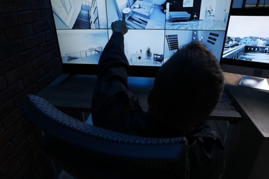 Photo of Security guard monitoring CCTV cameras in office at night, back view