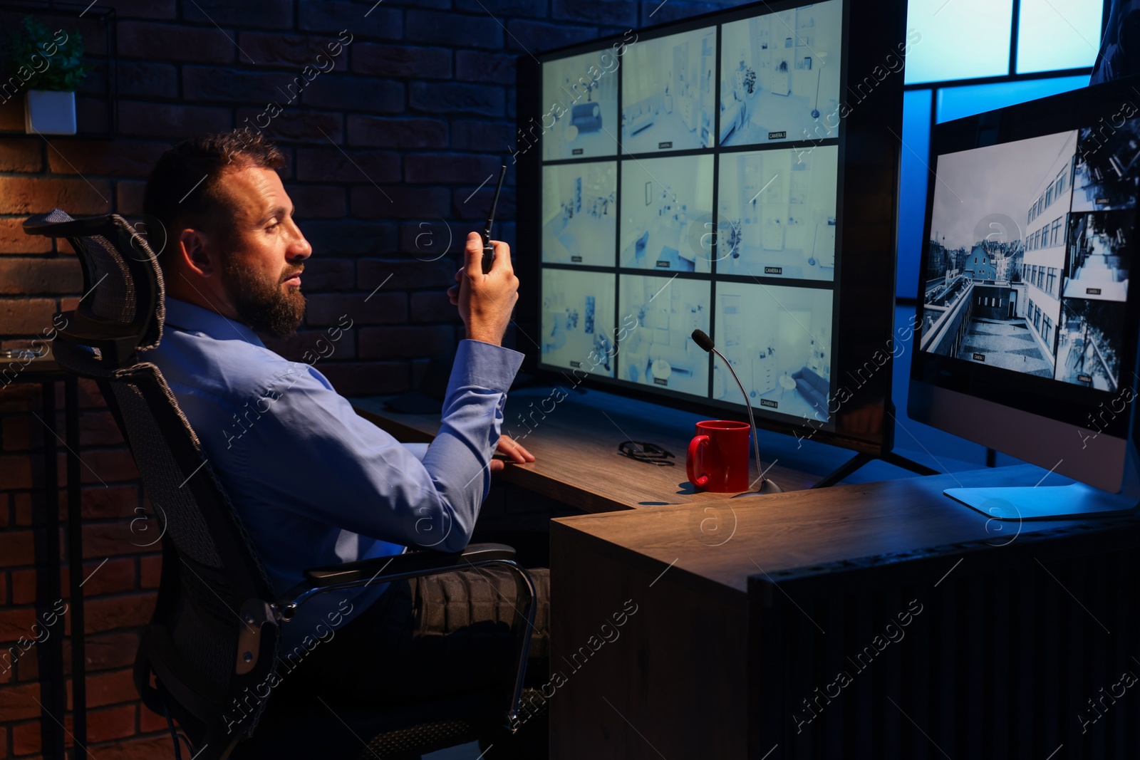 Security guard monitoring CCTV cameras and using walkie talkie in office at night Photo of Security guard monitoring CCTV cameras and using walkie talkie in office at night