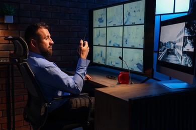 Photo of Security guard monitoring CCTV cameras and using walkie talkie in office at night