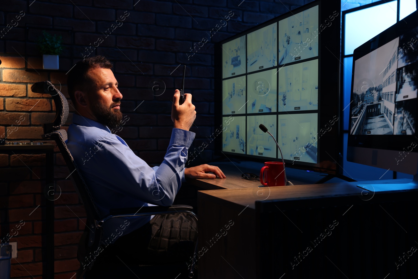 Security guard monitoring CCTV cameras and using walkie talkie in office at night Photo of Security guard monitoring CCTV cameras and using walkie talkie in office at night