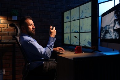 Photo of Security guard monitoring CCTV cameras and using walkie talkie in office at night