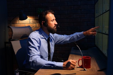 Photo of Security guard monitoring CCTV cameras in office at night