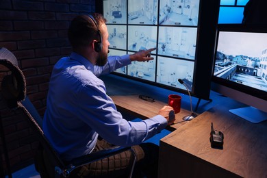 Photo of Security guard monitoring CCTV cameras in office at night, back view