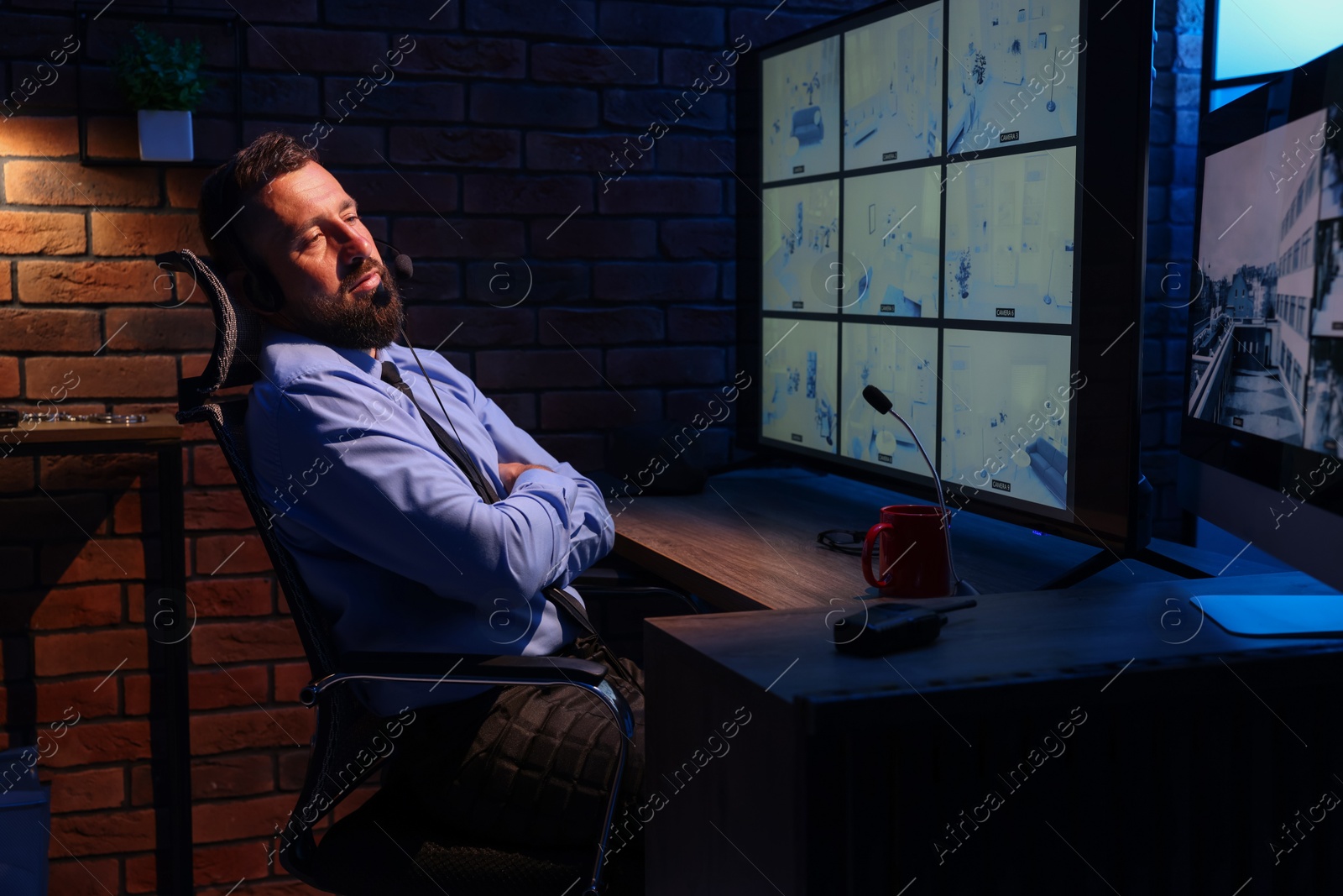 Tired security guard monitoring CCTV cameras in office at night Photo of Tired security guard monitoring CCTV cameras in office at night