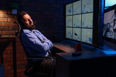 Photo of Tired security guard monitoring CCTV cameras in office at night