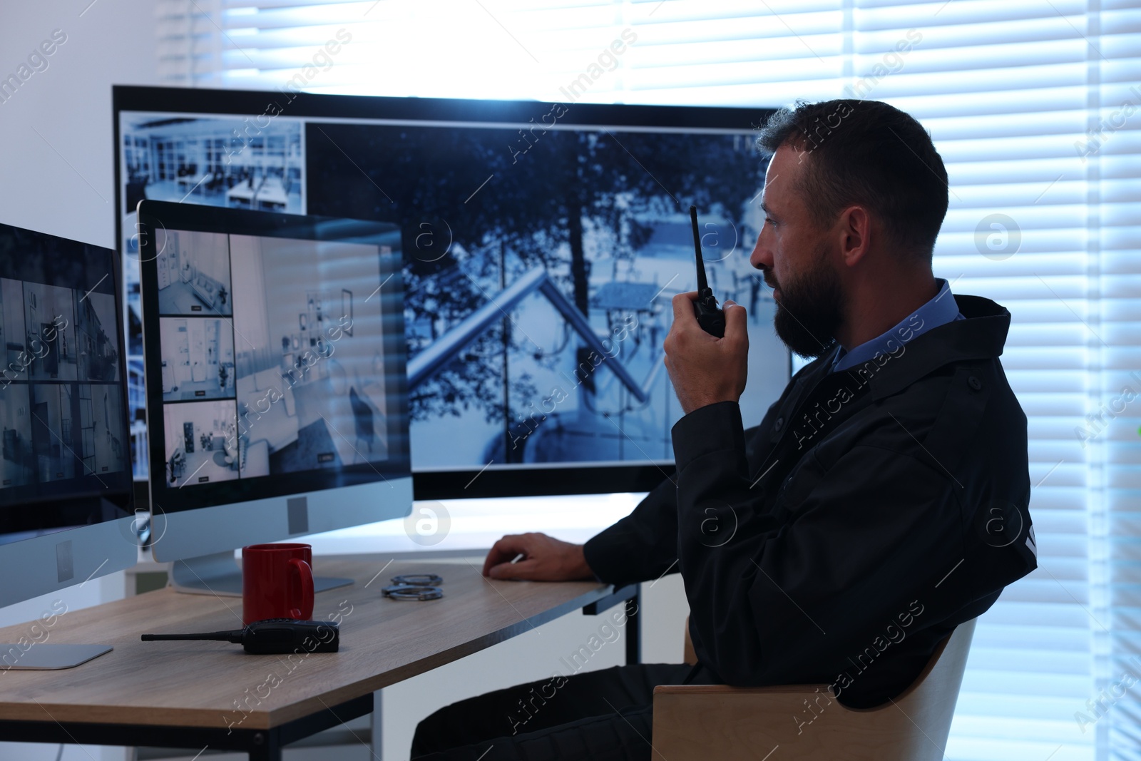 Security guard monitoring CCTV cameras and using walkie talkie in office Photo of Security guard monitoring CCTV cameras and using walkie talkie in office