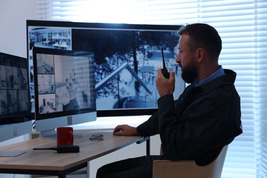 Photo of Security guard monitoring CCTV cameras and using walkie talkie in office