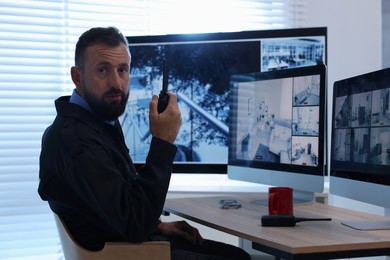 Photo of Security guard monitoring CCTV cameras and using walkie talkie in office
