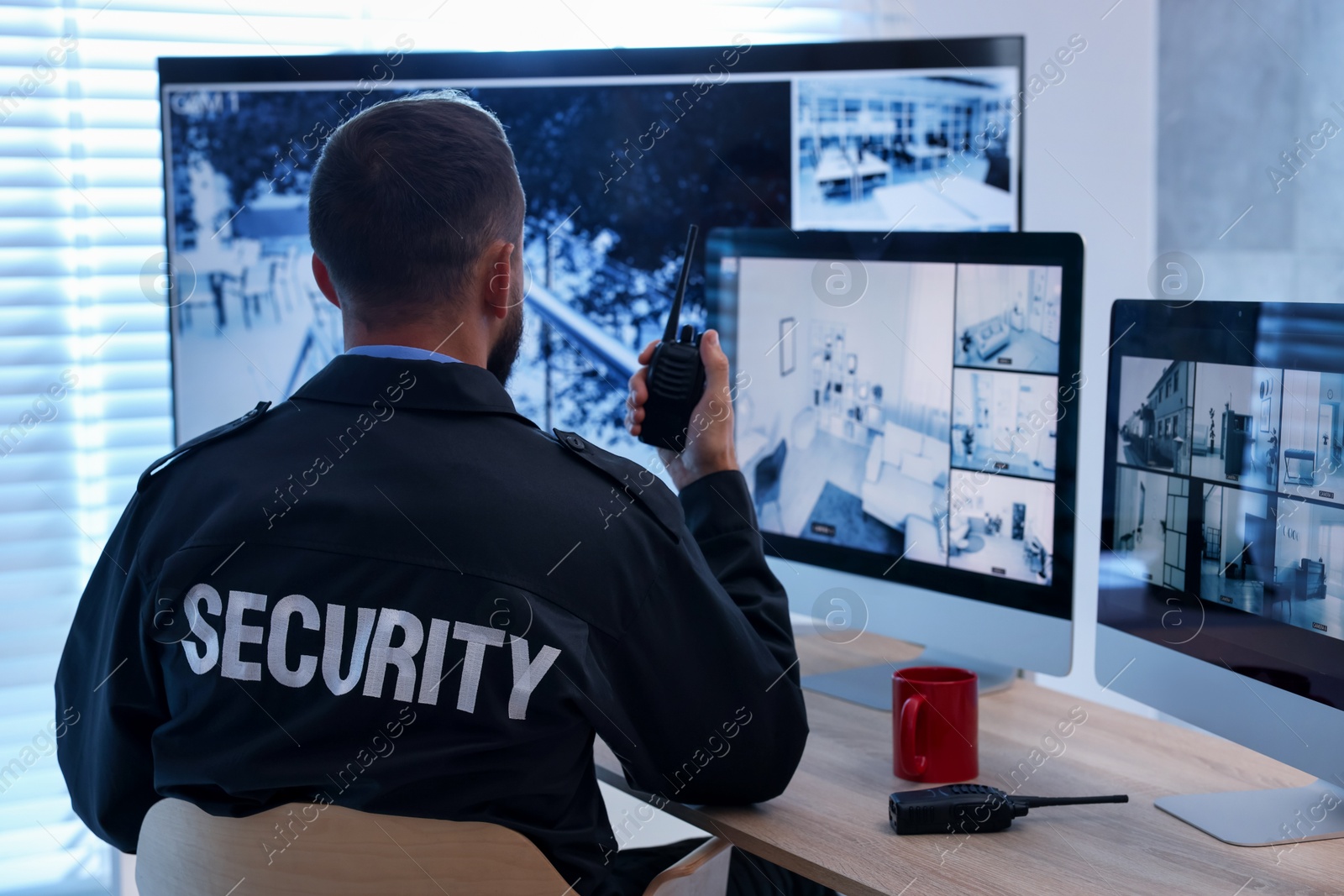 Security guard monitoring CCTV cameras and using walkie talkie in office, back view Photo of Security guard monitoring CCTV cameras and using walkie talkie in office, back view