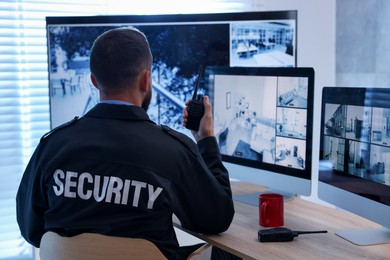 Photo of Security guard monitoring CCTV cameras and using walkie talkie in office, back view