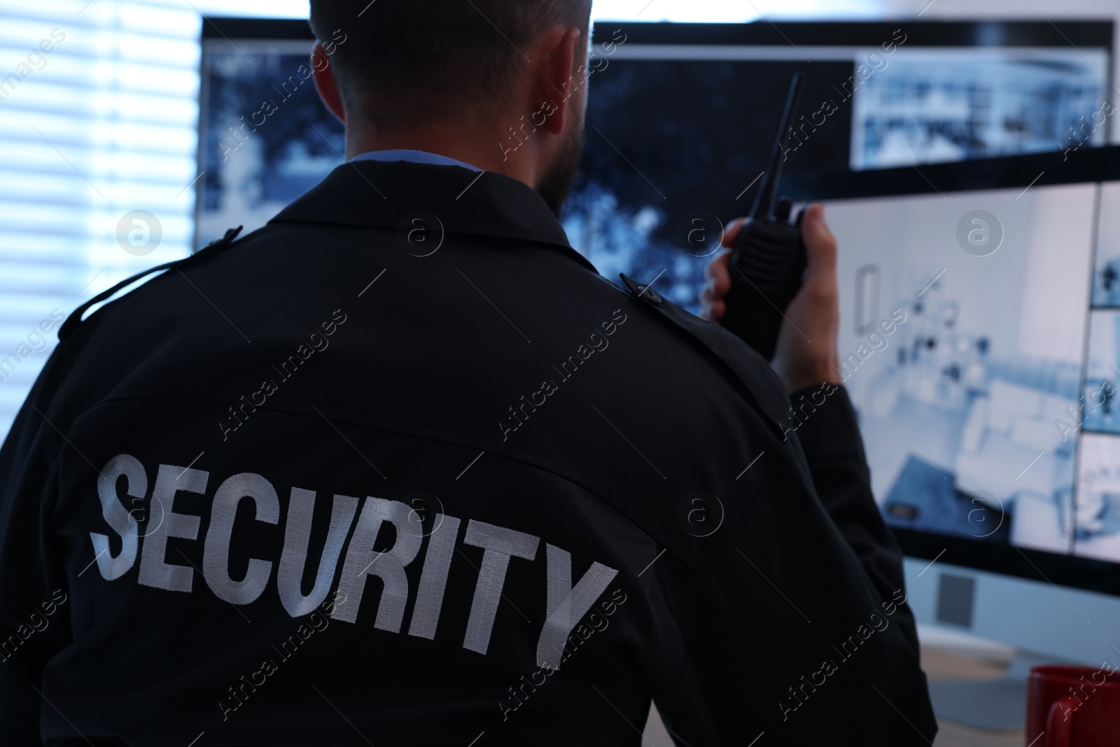 Security guard monitoring CCTV cameras and using walkie talkie in office, back view Photo of Security guard monitoring CCTV cameras and using walkie talkie in office, back view