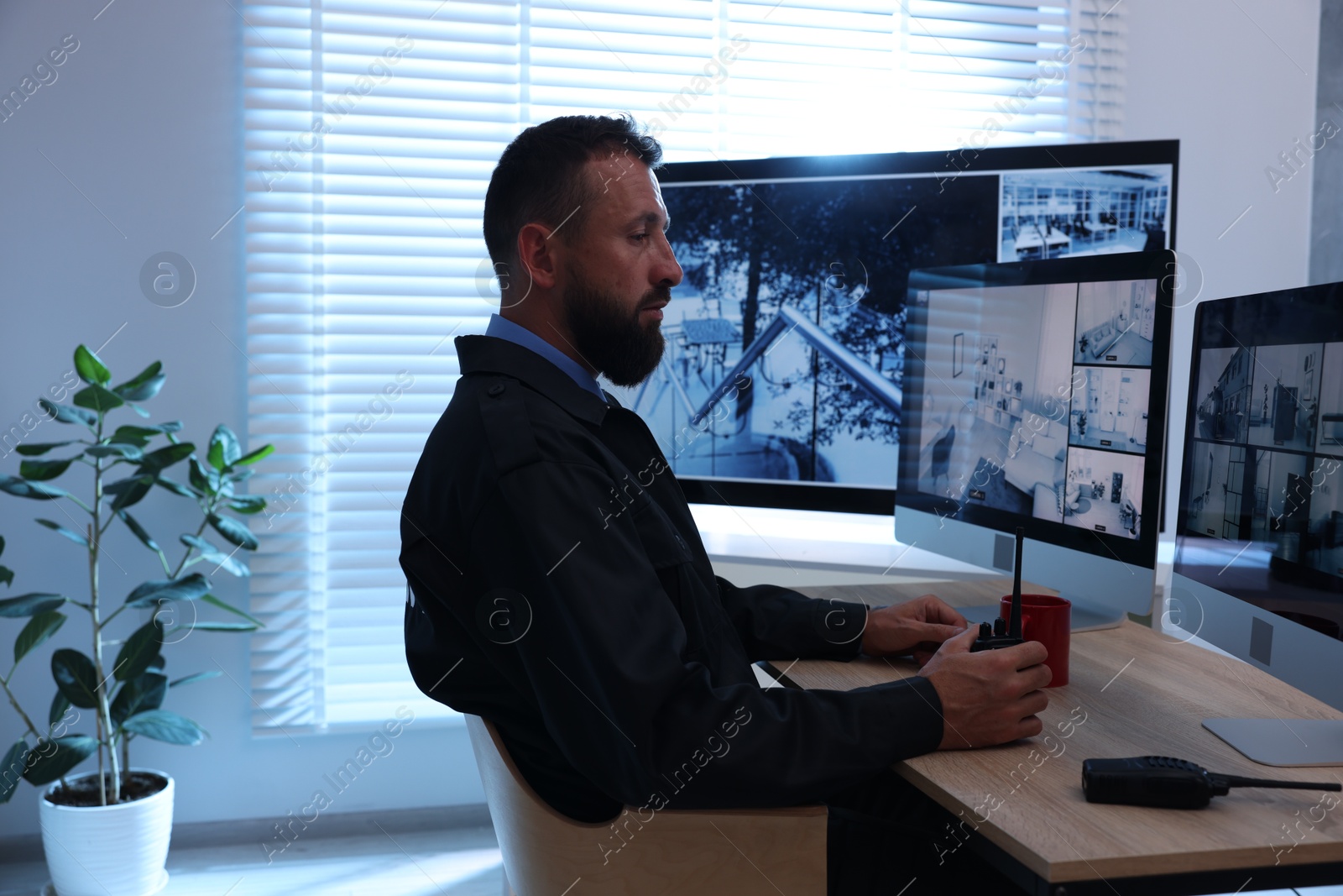 Security guard with walkie talkie monitoring CCTV cameras in office Photo of Security guard with walkie talkie monitoring CCTV cameras in office