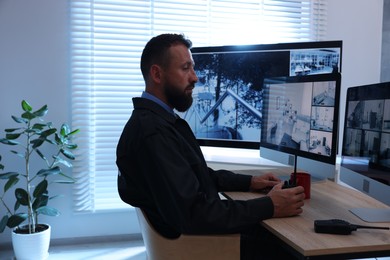 Photo of Security guard with walkie talkie monitoring CCTV cameras in office