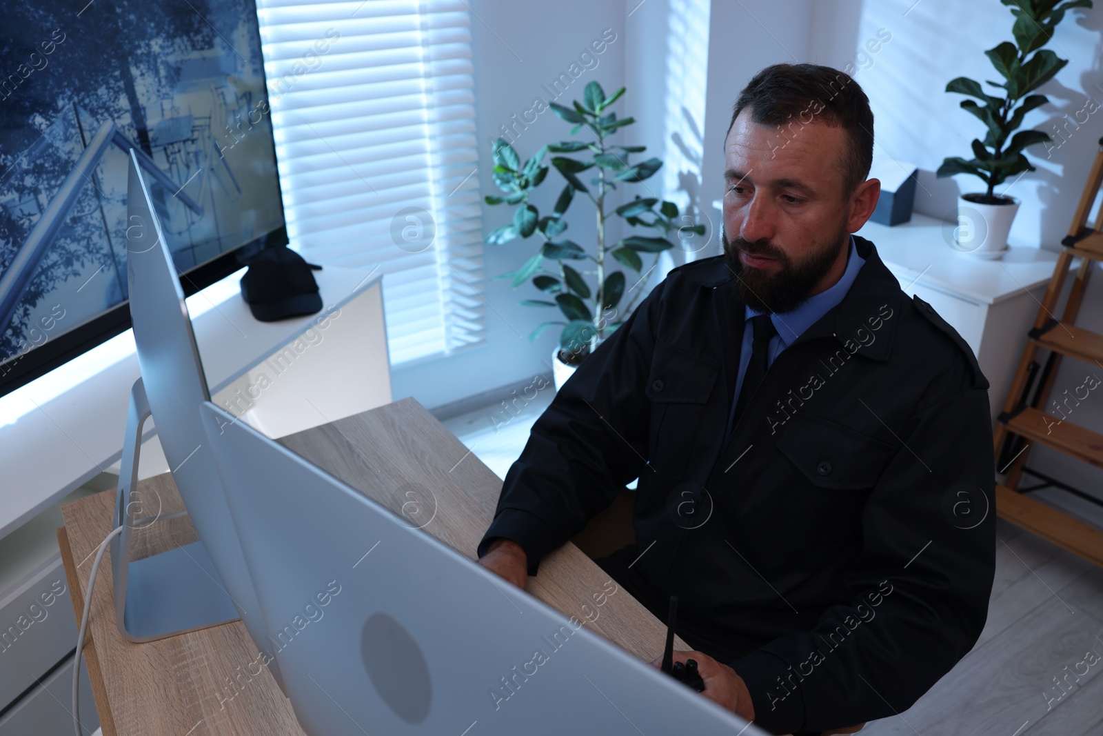 Security guard with walkie talkie monitoring CCTV cameras in office Photo of Security guard with walkie talkie monitoring CCTV cameras in office