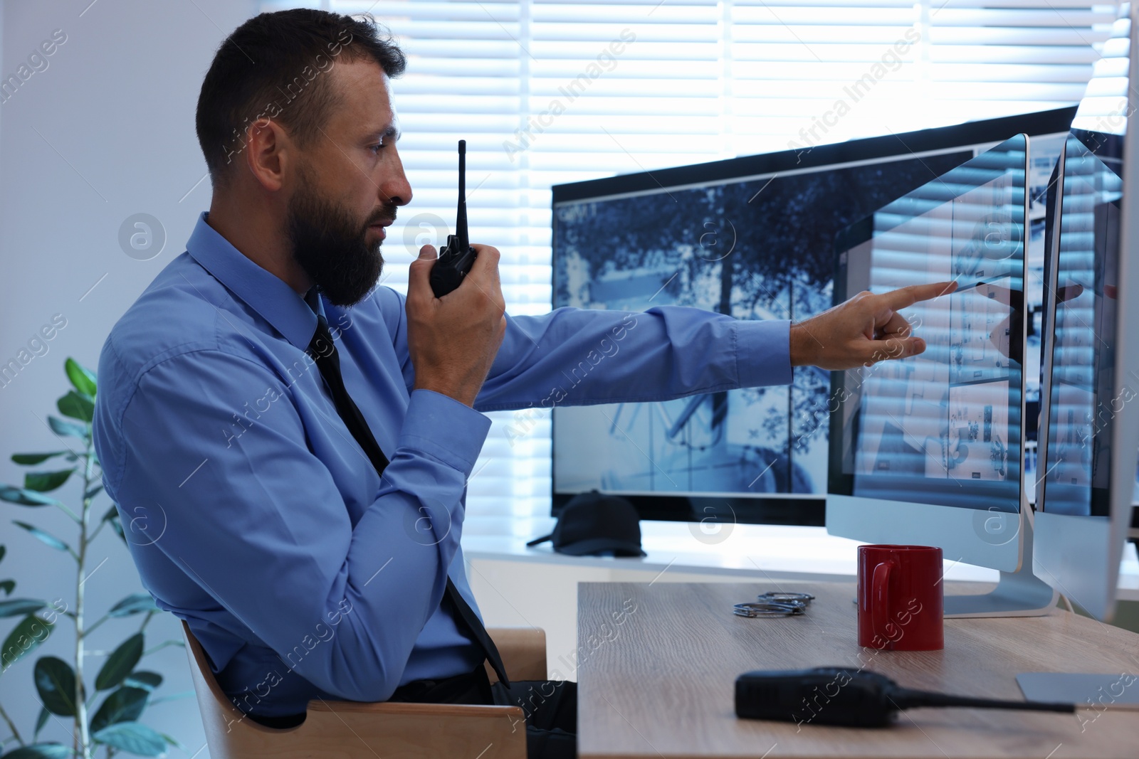 Security guard monitoring CCTV cameras and using walkie talkie in office Photo of Security guard monitoring CCTV cameras and using walkie talkie in office