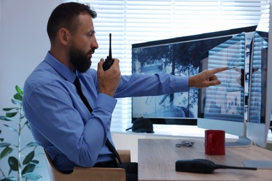 Photo of Security guard monitoring CCTV cameras and using walkie talkie in office