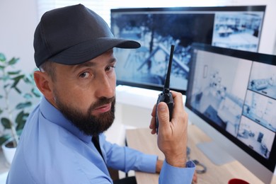 Photo of Security guard monitoring CCTV cameras and using walkie talkie in office