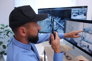 Photo of Security guard monitoring CCTV cameras and using walkie talkie in office