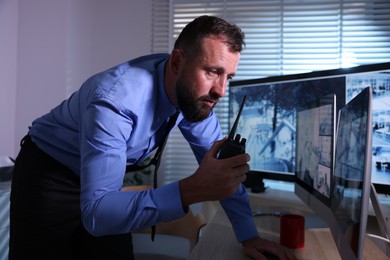 Photo of Security guard monitoring CCTV cameras and using walkie talkie in office