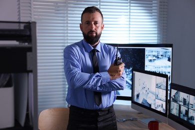 Photo of Security guard with walkie talkie near CCTV cameras in office
