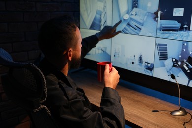 Photo of Security guard monitoring CCTV cameras in office at night, back view